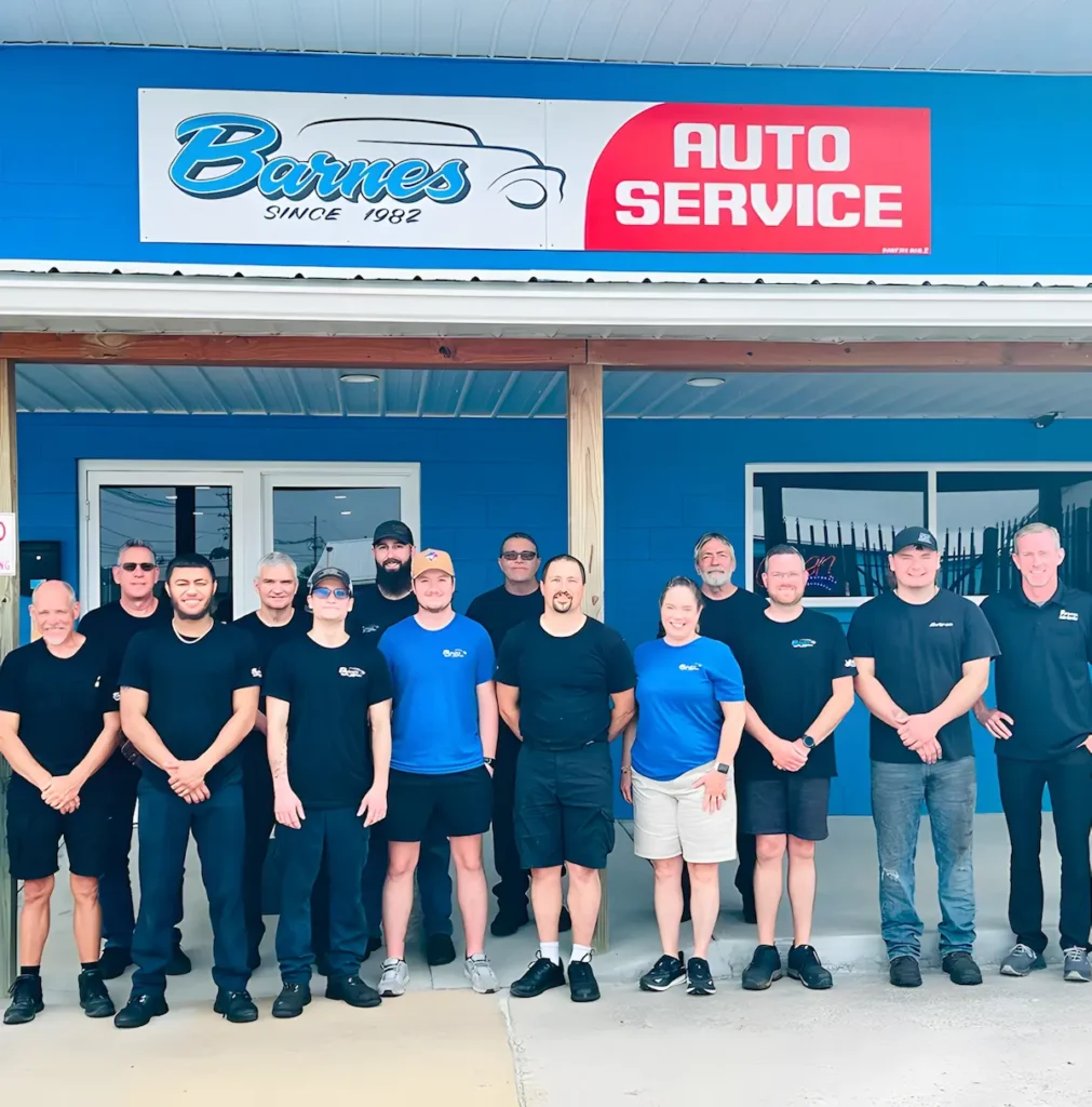 A group of 14 people, wearing mostly black or blue shirts, stand smiling in front of a blue building with a “Barnes Auto Service” sign above the entrance.