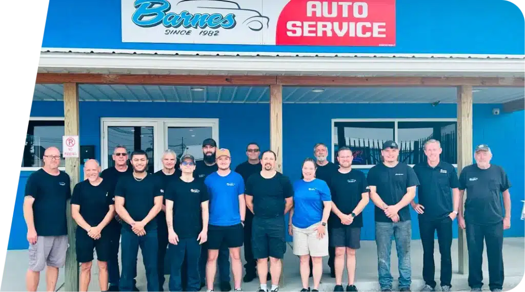 A group of fifteen people, mostly in black shirts, stand smiling in front of a blue building with a Barnes Auto Service sign above the entrance.