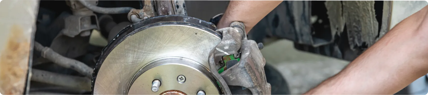Brake Repair In Louisville, KY At Barnes Auto Service. Close-up of a persons hands working on a cars exposed brake disc and caliper, performing maintenance or repairs on the vehicles braking system.