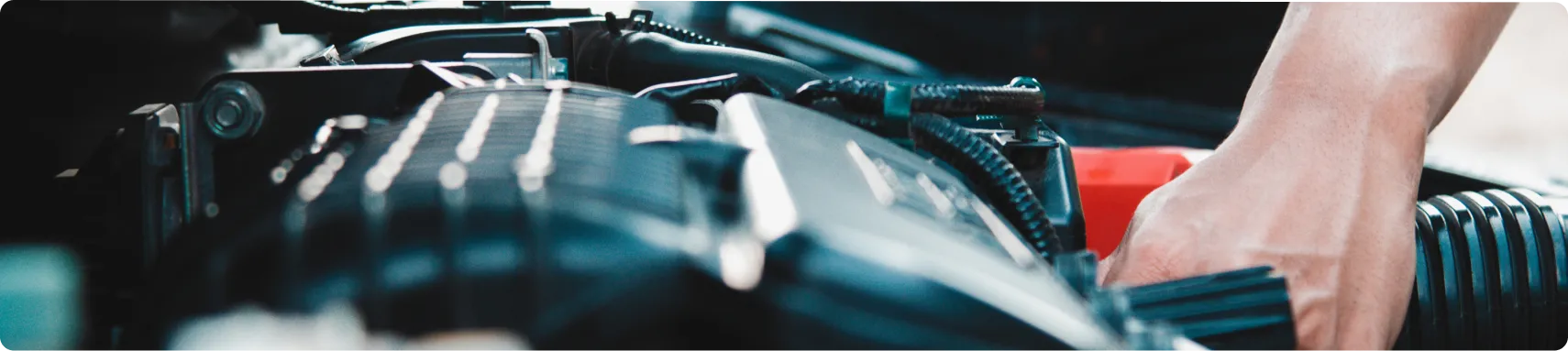 Engine Repair & Replacement In Louisville, KY At Barnes Auto Service. Close-up of a persons hand working on a car engine, surrounded by various engine components and wires under the hood.