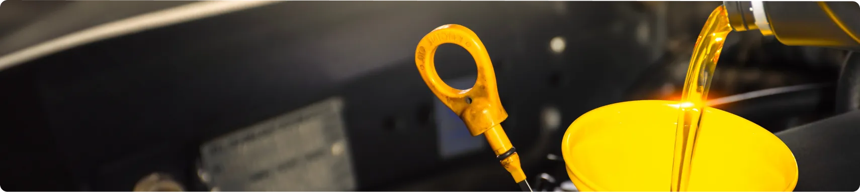 Oil Change In Louisville, KY At Barnes Auto Service. Golden motor oil is being poured from a bottle through a yellow funnel into a car engine, with the engine oil dipstick visible nearby.