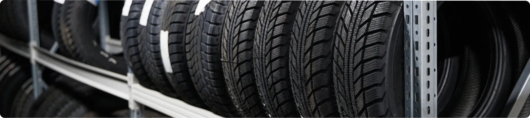 Tire Sales & Services In Louisville, KY At Barnes Auto Service. A row of black car tires with tread patterns is neatly stacked vertically on metal shelves in a tire shop or storage area.