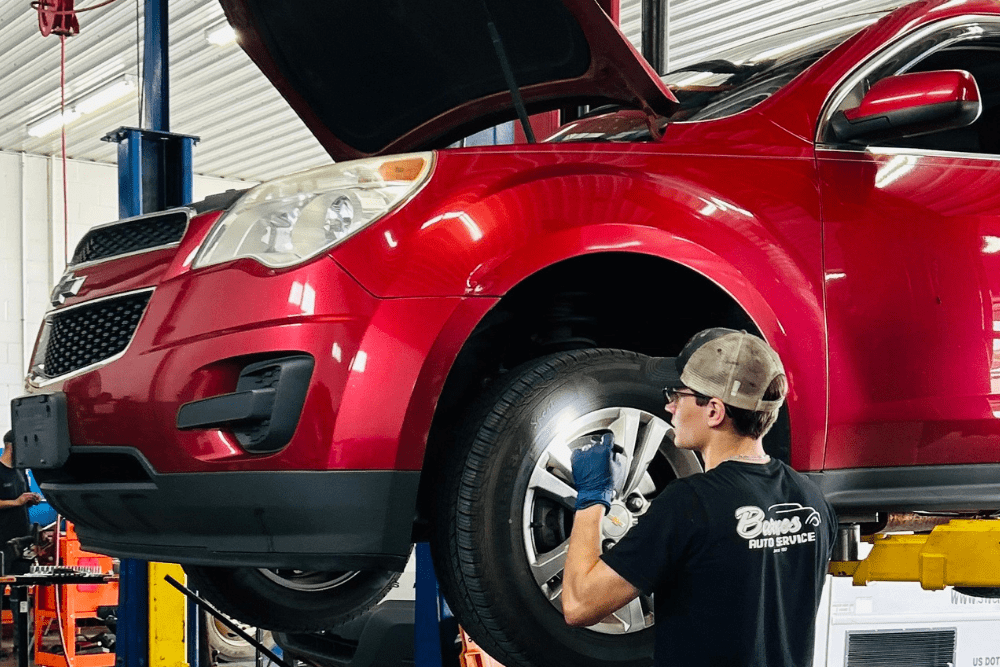 Brake services in Louisville, KY by Barnes Auto Service. Image of a mechanic inspecting the front suspension and brakes of a red Chevrolet SUV on a lift, showcasing hands-on expertise and precision in auto maintenance and repair.